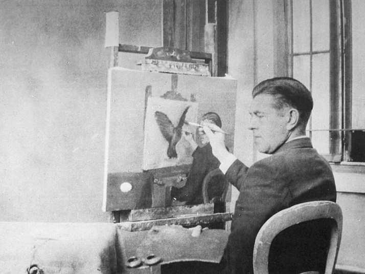 René Magritte fotografiado frente a uno de sus cuadros.